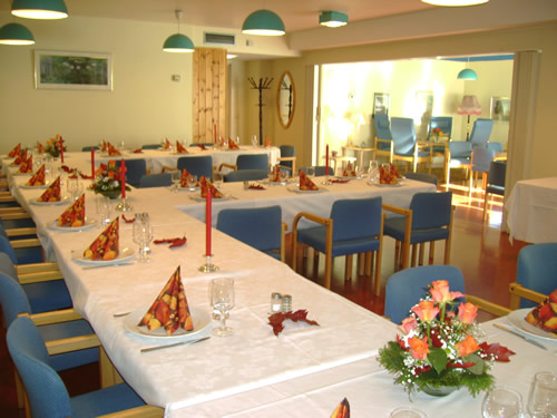 Bilde av et selskapslokale med bord med hvite duker dekket til middag og blå stoler